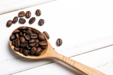 Beyaz ahşap arka planda ahşap kaşıkla kavrulmuş kahve çekirdekleri.