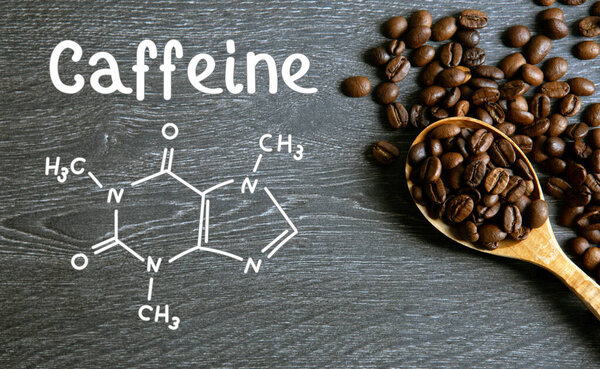 coffee beans with wooden spoon and chemical structure of caffeine on a wooden table