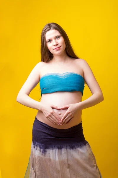 Woman hugging pregnant belly on the yellow background — Stock Photo, Image