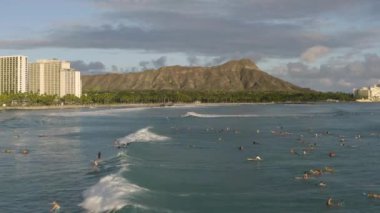 Aerial shot of a group of surfers riding a wave in Waikiki Beach with Diamond Head in the background