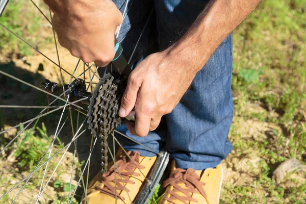 Kafkasyalı genç bir adamın mavi kot pantolon giydiği, evlerin arka bahçesinde dağ bisikletlerini tamir ettiği yakın plan görüntüsü.
