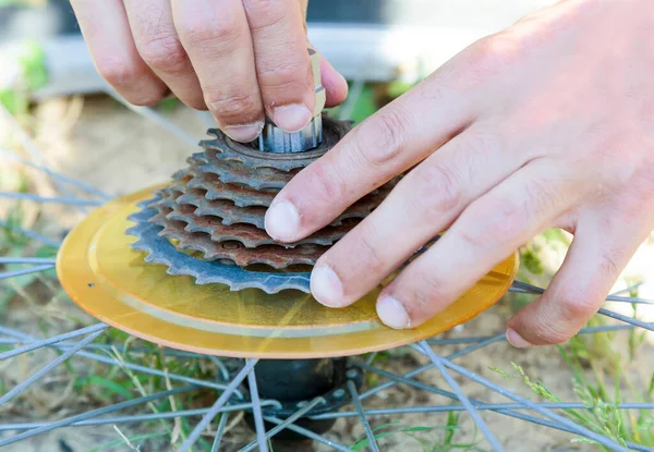 Kafkasyalı genç bir adamın yakın çekim görüntüsü, gün ışığında evlerin arka bahçesinde bir dağ bisikletinin dişlilerini ayarlıyor.