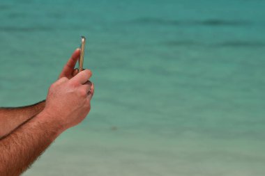 Tropikal kumsalda turkuaz su gölünde selfie çeken bir adam.