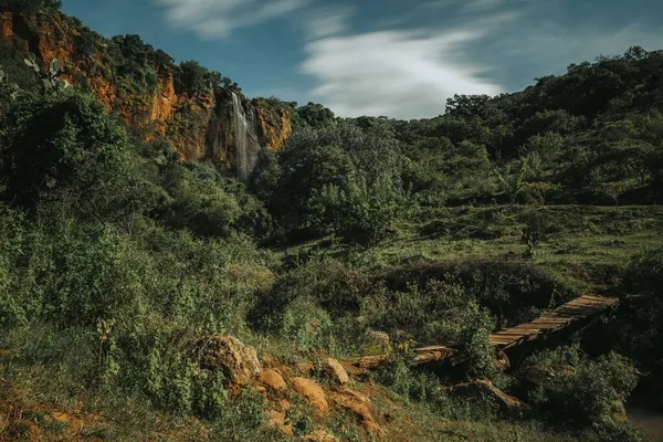森林中央的瀑布 从岩石上掉下来 穿过一条小河 带着云彩的长期曝光摄影 — 图库照片