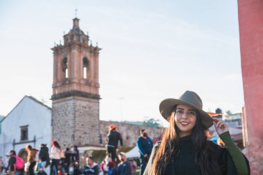 Maceracı kız, Tlalpujahua, Meksika 'nın Büyülü Kasabası' nı keşfediyor. Caddelerine ve klasik Meksika mimarisinin kiliselerine hayranlıkla gülümsüyor. Siyah panço ve yeşil şapka takıyor..