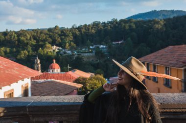 Maceracı kız, Tlalpujahua, Meksika 'nın Büyülü Kasabası' nı keşfediyor. Caddelerine ve klasik Meksika mimarisinin kiliselerine hayranlıkla gülümsüyor. Siyah panço ve yeşil şapka takıyor..