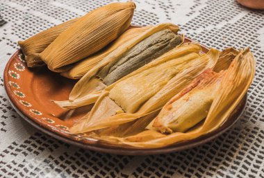 Sweet pineapple tamales, blue and red chili tamales. Typical Mexican food. On a clay plate and accompanied by corn.