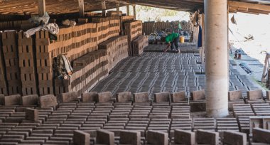 İşçi, yakın zamanda yapılmış tuğlaları, açık havada kuruyabilmeleri ve daha sonra fırınlarda ateşlenebilmeleri için düzenliyor..