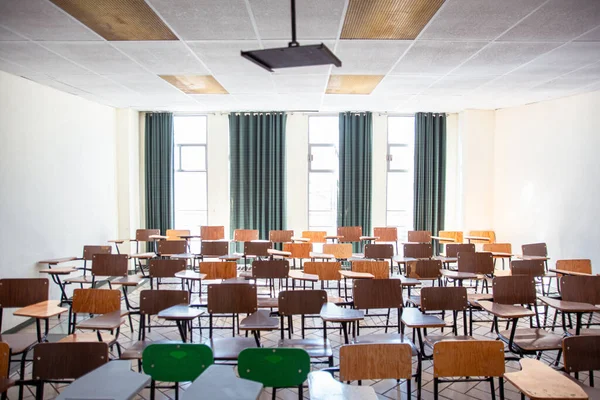 Farklı renkte masaları olan boş sınıf, doğal ışıklandırma için büyük pencerelerin arkasında.