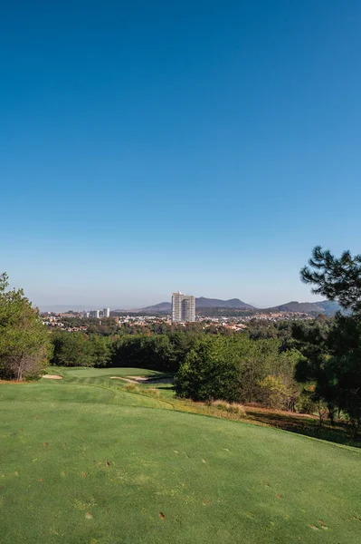 Golf course landscape with short green grass, some hills and trees.