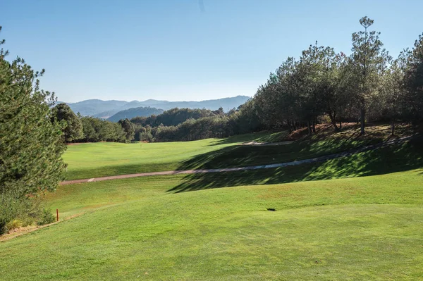 Golf course landscape with short green grass, some hills and trees.