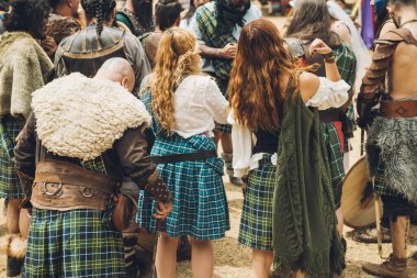 Medieval Scottish warriors in a meeting to discuss battle tactics, all in the colors characteristic of their clans, using their kilts to differentiate themselves.