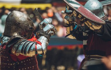 Ortaçağ şövalyelerinin çarpışması. Kendilerini savunmak için metal zırhlar, baltalar, kılıçlar ve kalkanlar kullanıyorlar..