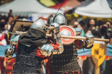 Ortaçağ şövalyelerinin çarpışması. Kendilerini savunmak için metal zırhlar, baltalar, kılıçlar ve kalkanlar kullanıyorlar..