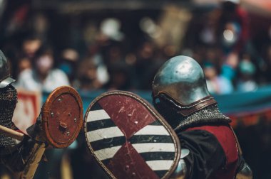 Ortaçağ şövalyelerinin çarpışması. Kendilerini savunmak için metal zırhlar, baltalar, kılıçlar ve kalkanlar kullanıyorlar..