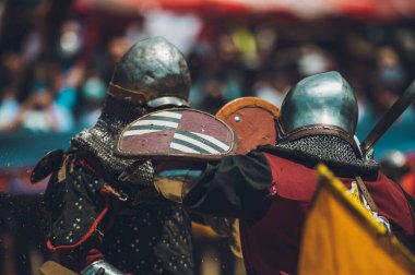 Ortaçağ şövalyelerinin çarpışması. Kendilerini savunmak için metal zırhlar, baltalar, kılıçlar ve kalkanlar kullanıyorlar..