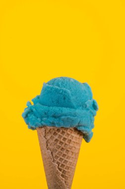 Bubble gum ice cream in a traditional cone on a yellow background.