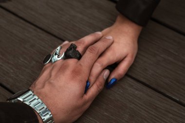 Wedding couple hold hands, his hand covers hers and their colorful rings stand out