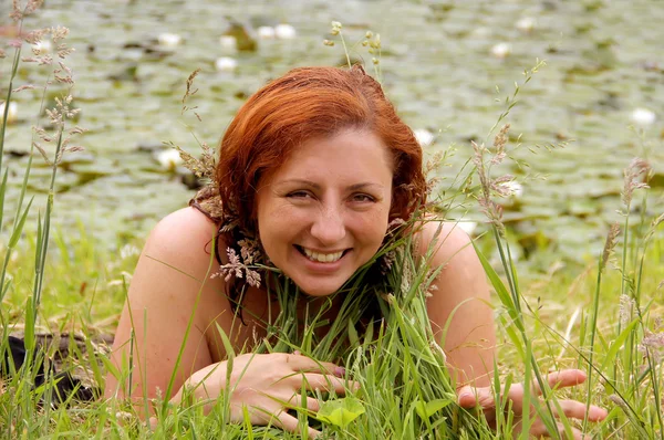 Vacker rödhårig kvinna om i gräset vid sjön — Stockfoto