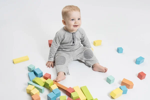 Joyful baby plays with a wooden blocks, educational toys on the floor. White studio background. Early childhood development, safe paints for toys, 6-12 months old children skills, Montessori concept.