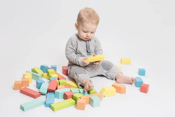 Interested baby plays with wooden blocks, educational toys on white studio background. Early childhood development, toddler skills, safe paints for wooden toys, Montessori, kindergarten concept.