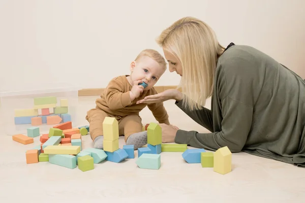 Çocuk yerdeki tahta oyuncaklarla oynuyor. Bebeğin ağzında oyuncağın bir parçası vardı, annesi almak için elini uzattı. Erken gelişim kavramı, bebek oyuncaklarını ağzına alır, boğulma tehlikesi