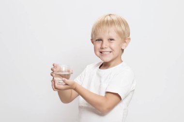 Bir bardak suyla yakışıklı beyaz bir çocuk. Gülen surat. Beyaz arka plan. Çocuklar tarafından içilebilir temiz su kavramı, su kaynakları ve içme suyu sorunu. Boşluğu kopyala