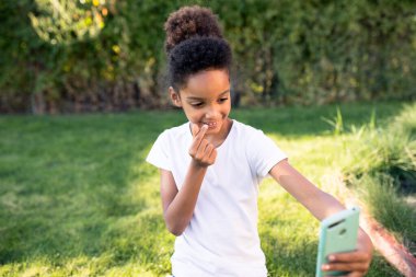 Sevimli bir kız küçük bir kalp atışı yapıyor ve el işareti gösteriyor. Telefonunun ön kamerasında kendini çekiyor. Çocuk kalp yaptı, parmaklarıyla hareket etti. Otantik bir an. Yaşam biçimi. 