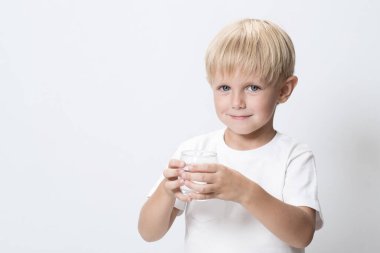 Beyaz tatlı bir çocuk, bir bardak suyla sarışın bir çocuk. Beyaz stüdyo geçmişi. Çocuklar tarafından içilebilir temiz su kavramı, su kaynakları ve içme suyu sorunu. Boşluğu kopyala