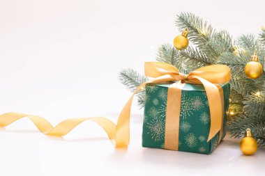Noel kutlaması, beyaz arka planda altın küreli yeni yıl kompozisyonu, yeşil kağıda sarılı hediye kutusu ve altın bir kurdele ve çelenk ışıklı dekoratif bir dal. Metnin için boşluk kopyala.