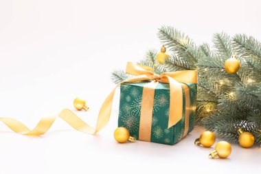 Noel kutlaması, beyaz arka planda altın küreli yeni yıl kompozisyonu, yeşil kağıda sarılı hediye kutusu ve altın bir kurdele ve çelenk ışıklı dekoratif bir dal. Metnin için boşluk kopyala.