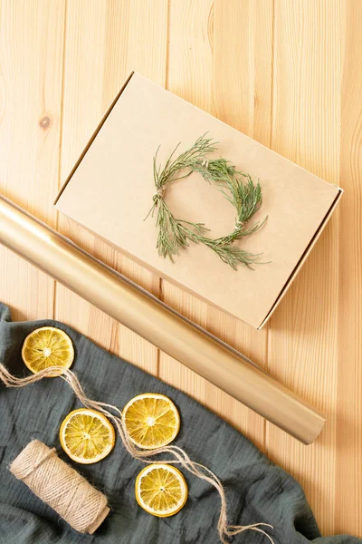 Concept of original idea, eco friendly materials for wrapping Christmas gifts. Craft box, whip, green twigs, wrapping paper, dried orange, muslin cloth on wooden table. Step-by-step instruction. Step1