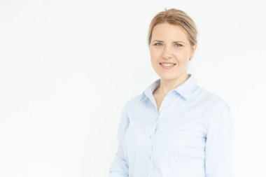 Beyaz duvar arkasında poz veren kendinden emin genç bir kadının portresi. Mavi gözlü mutlu sarışın kız. Mavi gömlek. Doğal güzellik, kadın cinselliği, iş saç stili konsepti. Boşluğu kopyala