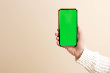 Yeşil akıllı telefon ekran modelini tutan bir kadın el. Modern cep telefonu. Bej renkli stüdyo. Yakın plan. Modern teknolojiler, çevrimiçi ticaret, mobil uygulama, sosyal ağlar konsepti.