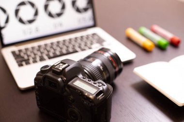 Kamera dizüstü bilgisayarın klavyesinde, arka planda da koyu tahta masa var. Ekranda diyafram açıklığı. Çevrimiçi kurslar kavramı, temel fotoğrafçılık eğitimi, fotoğrafçılık mesleği, içerik.