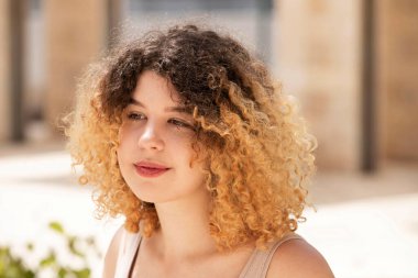 Mutlu bir kızın portresi. - Dışarıda. Kıvırcık saçlı, açık tenli güzel genç kız rüya görüyor, nefes alıyor. Güneşli bir gün.