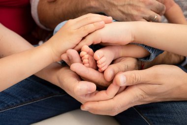 Yeni doğmuş bir bebeğin, yetişkinlerin ve çocukların, büyük bir ailenin bacaklarının etrafındaki eller. Kapatın. Kavram birlikte, mutluluk, aile değerleri, ebeveynlik, çocukluk, destek.