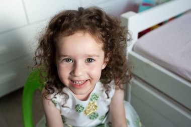 Gülümseyen küçük bir kızın yakın plan portresi. 4 yaşında, güzel yeşil gözlü, kıvırcık saçlı. Göz teması. 