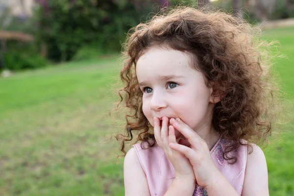 Dışarıda dört yaşında neşeli bir çocuğun portresi. Yeşil çimenler, arka tarafa park et. Şirin kıvırcık beyaz kız. Bir çocuğun gülen yüzü. Sağlık anlayışı, çocuklar, diş tebessümü, süt dişleri.