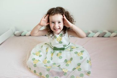 Tatlı, pozitif çocuk yatakta oyun oynuyor. Kıvırcık 4 yaşındaki kız ellerini kullanarak saklambaç oynuyor. Çocuklarla oynama kavramı, çocukluk, kız çocuğu, vizyon.