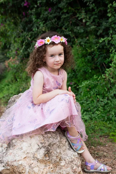 Маленька Дівчинка Кучерявим Волоссям Красивій Рожевій Сукні Вінком Квітів Сидить — стокове фото