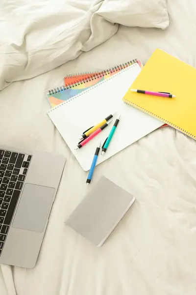 办公用品或学习用品 文具都放在笔记本电脑旁边的床上 没人彩色钢笔 笔记本 笔记本 家庭学习 远程工作 在线教育 远程教育 电子商务的概念 图库图片