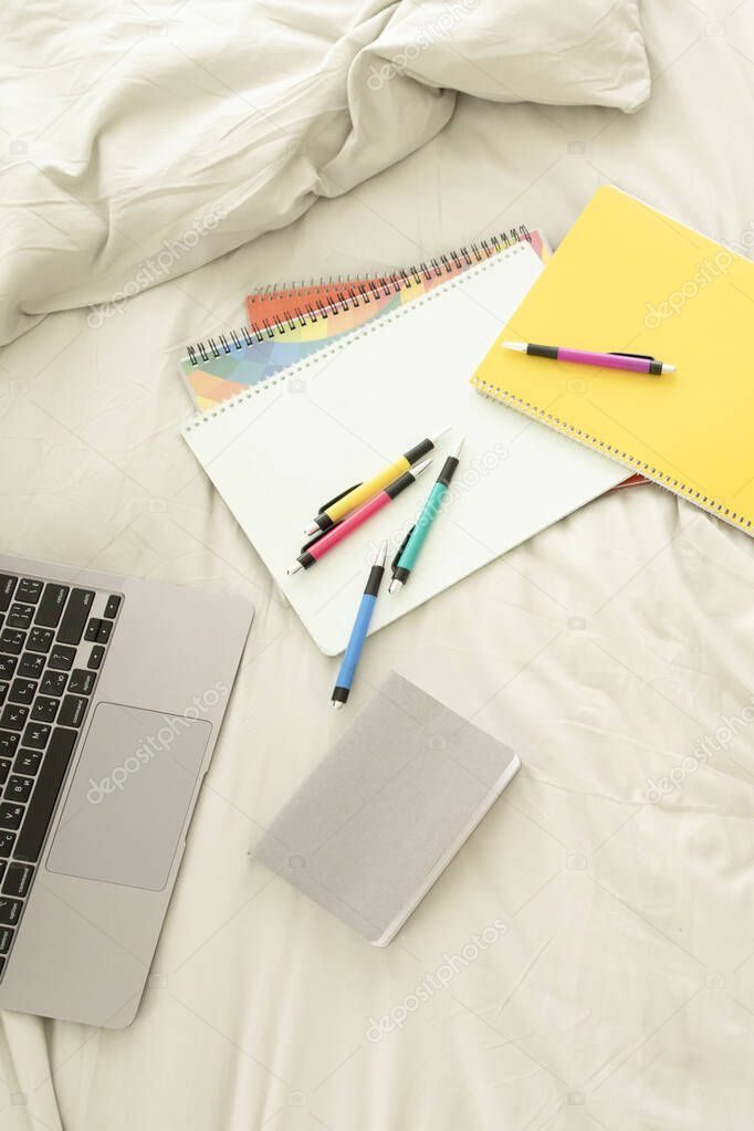 Office or school supplies, stationery lie on the bed next to the laptop. Nobody. Colored pens, notebooks, notepad. Concept of homeschooling, remote work, online education, distance school, e-business.