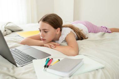 Evde, yatak odasında dizüstü bilgisayarın önünde üzgün bir kız. Üzgün surat. Kız yorgun, online ders dinlemekten sıkılmış. Evde eğitim kavramı, uzaklık eğitimi, eğitim, okul çocukları.
