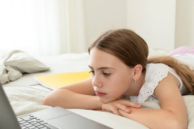Evde, yatak odasında dizüstü bilgisayarın önünde üzgün bir kız. Üzgün surat. Kız yorgun, online ders dinlemekten sıkılmış. Evde eğitim kavramı, uzaklık eğitimi, eğitim, okul çocukları.