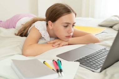 Evde, yatak odasında dizüstü bilgisayarın önünde üzgün bir kız. Üzgün surat. Kız yorgun, online ders dinlemekten sıkılmış. Evde eğitim kavramı, uzaklık eğitimi, eğitim, okul çocukları.