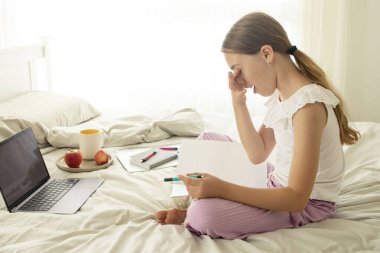 Girl 10 years old sitting in front of a computer screen rubs her eyes.  Schoolgirl has sore eyes, vision problems. Concept of kids and gadgets, screen time, learning, distance education, home school. 