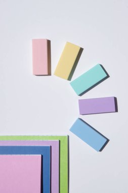 Silgi ve not defterlerinin renklerle dolu orijinal bir kompozisyonu. Beyaz arka plan. Okul teması. Eğitim konsepti, okula dönüş, sanat, soyutlama, kırtasiye. Uzayı kopyala Üst görünüm.