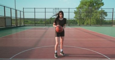 Genç bir kız basketbol oyuncusu okul kortunda antrenman yapıyor ve egzersiz yapıyor. Beyaz çoraplı genç bir kadın basketbol topuyla çapraz atlama eğitimi alıyor.