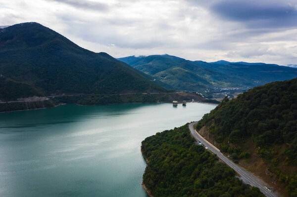 A road near the Zhinvali Reservoir in Georgia. Georgian military road from Tbilisi to Kazbegi. Panorama of the lake in the mountains. Beautiful blue lake between the mountains with clouds in the sky